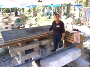 Ann standing next to her chest of tools and her latest slate stone sculpture of crows under a pop up canopy.